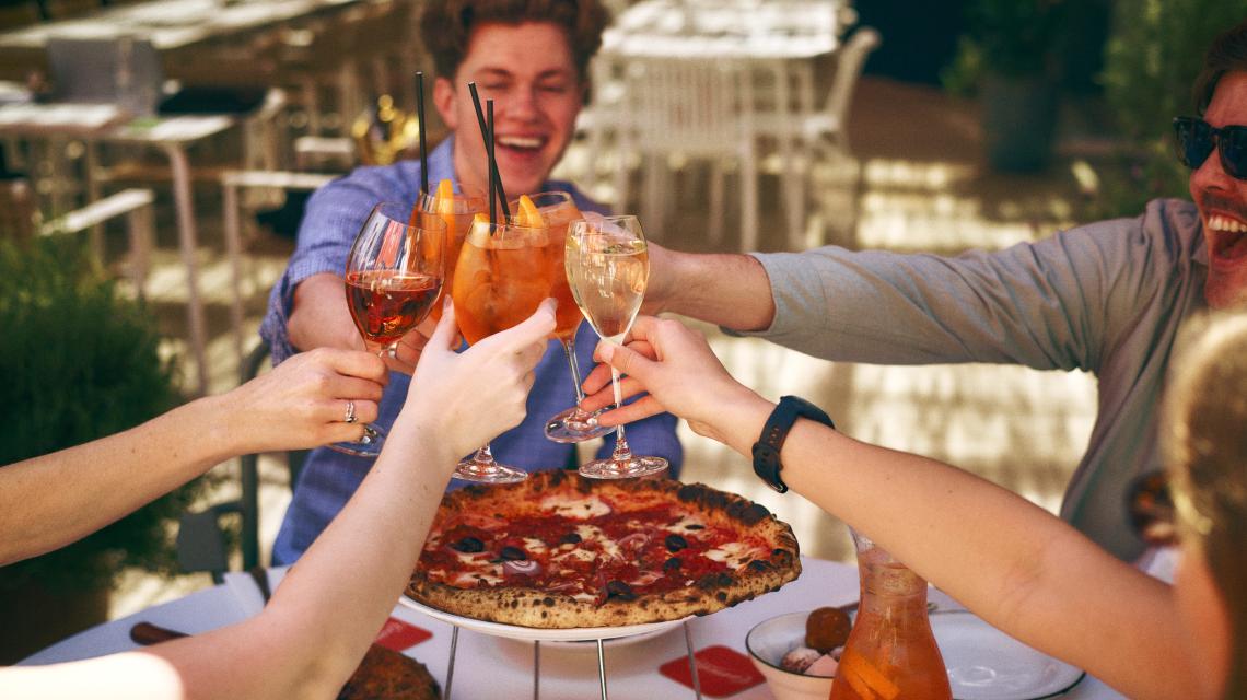 Spritzes raised over pizza in the courtyard