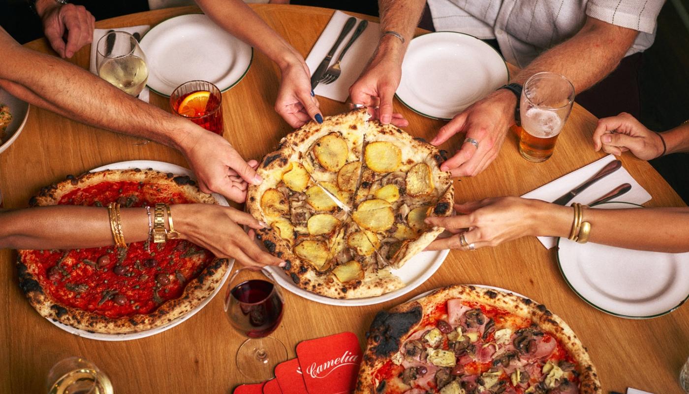 Hands reaching for wood-fired pizzas