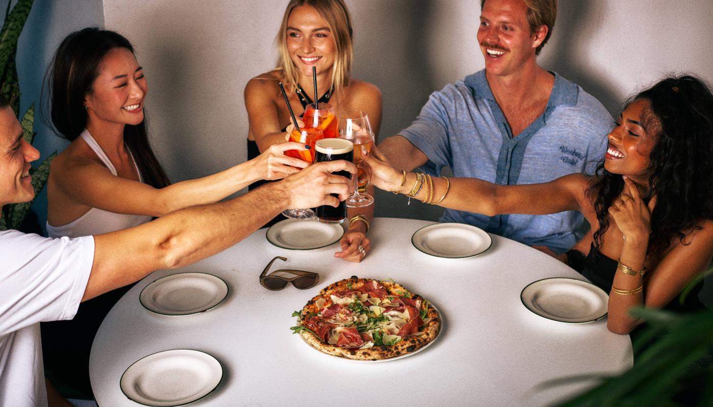 Friends toasting spritzes over pizza