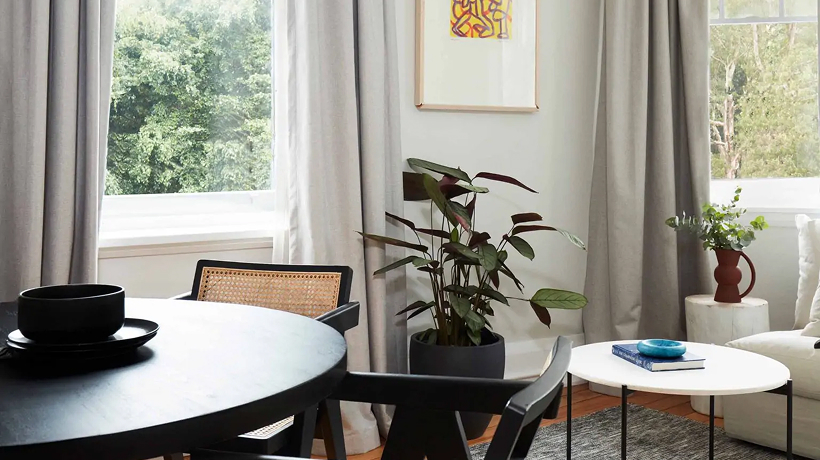 Heritage apartment living room — round dining table, rattan chairs and a leafy outlook
