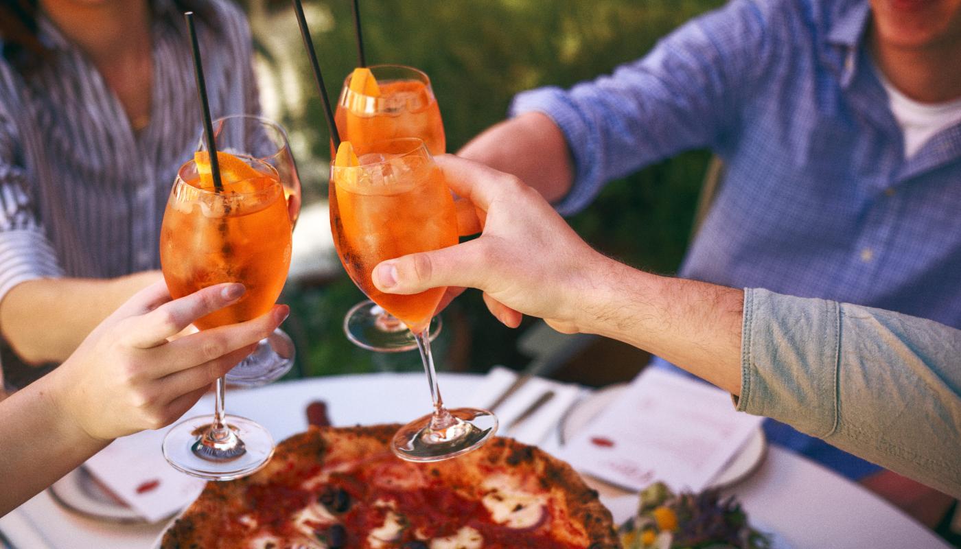 Spritzes clinking over a wood-fired pizza
